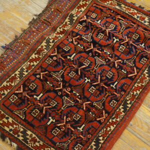 Low-pile scatter rug with complex geometric motifs in rust, navy, and ivory on worn wood planks.