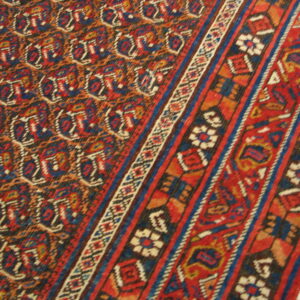 Dense red and blue rug with repeating geometric patterns and multi-banded striped borders.