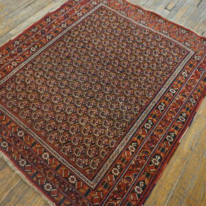 Red and navy traditional rug with dense repeating patterns and multiple borders on rustic wood plank flooring.