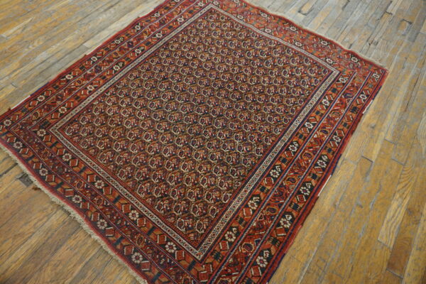 Red and navy traditional rug with dense repeating patterns and multiple borders on rustic wood plank flooring.