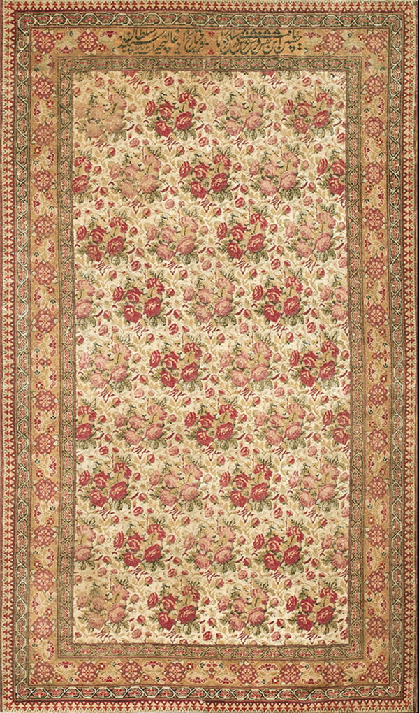 Beige rug featuring a dense red rose pattern, ornate tan borders, and visible calligraphy along the top edge.