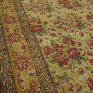 Red and pink roses cover a gold floral rug field next to a defined geometric border on wood planks.