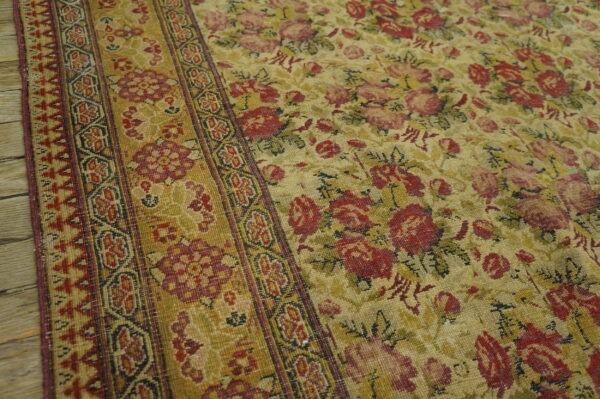 Red and pink roses cover a gold floral rug field next to a defined geometric border on wood planks.