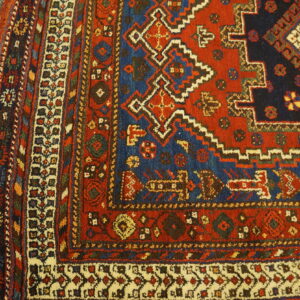 Geometric red, navy, and ivory rug corner showing low pile and multiple borders on wood floors.