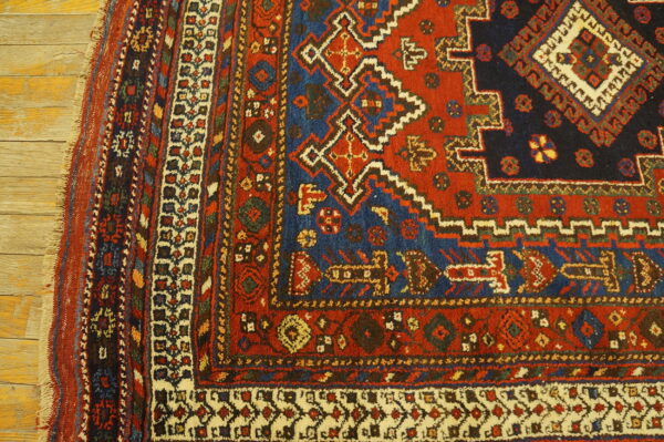 Geometric red, navy, and ivory rug corner showing low pile and multiple borders on wood floors.