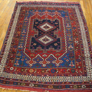 Red and blue geometric rug with a central medallion on light-colored wood plank flooring.