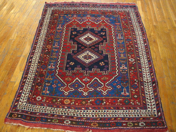 Red and blue geometric rug with a central medallion on light-colored wood plank flooring.