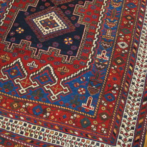 Geometric traditional rug in rich red, navy, and blue tones, shown next to glossy wood flooring.