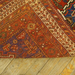 Tightly woven geometric rug reverse side, featuring orange, blue, and cream colors, rests on wood planks.