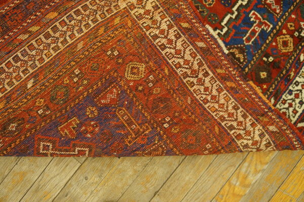Tightly woven geometric rug reverse side, featuring orange, blue, and cream colors, rests on wood planks.