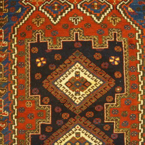Detailed view of a geometric rug featuring a navy stepped medallion on a rust red field.
