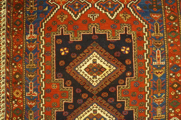 Detailed view of a geometric rug featuring a navy stepped medallion on a rust red field.