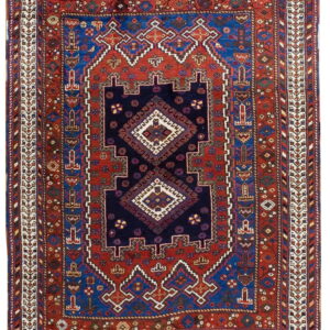 Geometric rug in navy, bright blue, and rust red, featuring a centralized diamond design and complex borders.