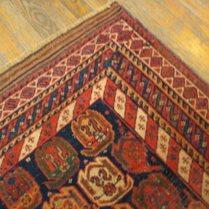 Geometric patterned rug corner in red, dark blue, and cream sits on worn golden wood planks.