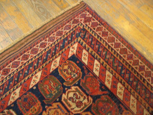 Geometric patterned rug corner in red, dark blue, and cream sits on worn golden wood planks.