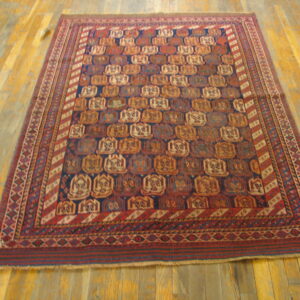Geometric rug in deep red and navy with tan motifs laid on golden-toned hardwood planks.