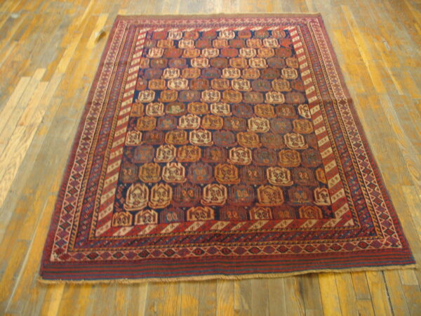 Geometric rug in deep red and navy with tan motifs laid on golden-toned hardwood planks.