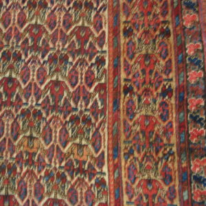 Geometric rug detail featuring repeating red, blue, and cream motifs with a multi-layered border on wooden flooring.