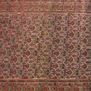 Close-up view of a traditional rug with complex red, blue, and cream geometric patterns and layered borders.