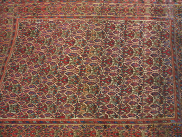 Close-up view of a traditional rug with complex red, blue, and cream geometric patterns and layered borders.