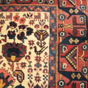 Woven rug detail showing a cream field with navy and red animal motifs next to a thick red geometric border.