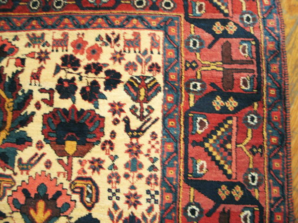 Woven rug detail showing a cream field with navy and red animal motifs next to a thick red geometric border.