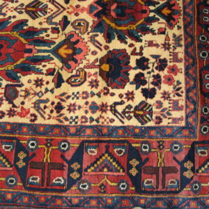 Detail of a traditional rug featuring a high pile and complex red, navy, and cream floral and geometric patterns.