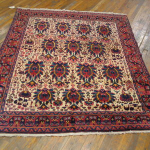 Low-pile rug features red borders and a cream field with navy and red repeating medallions on wood flooring.