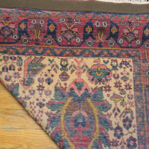 A colorful, low-pile traditional rug is folded on a wood floor, exposing its backing and intricate pattern.