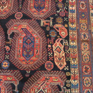 Navy and red patterned rug with stylized animals and geometric guls shown next to hardwood flooring.