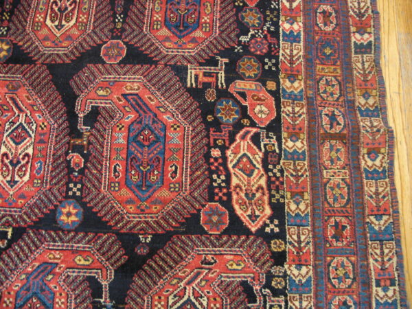 Navy and red patterned rug with stylized animals and geometric guls shown next to hardwood flooring.