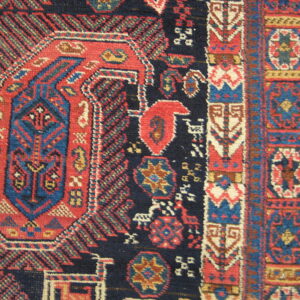 Intricate close-up of a rug pattern with a navy field, red central medallion, and blue geometric borders.