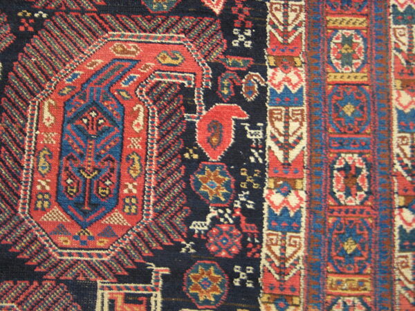 Intricate close-up of a rug pattern with a navy field, red central medallion, and blue geometric borders.