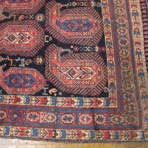 Navy rug with repeating red and blue geometric patterns and fringed edges on wood floor.