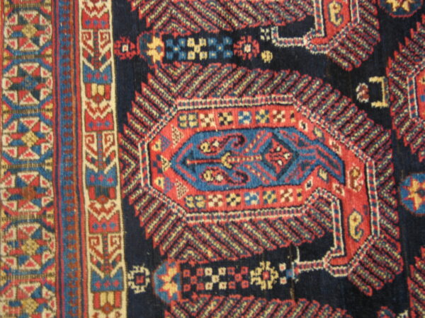 Geometric rug pattern featuring a navy field, a red and blue central motif, and complex multicolored borders.