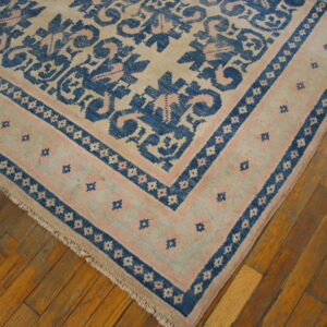 Low-pile rug with geometric patterns in cream, blue, and pale pink rests on warm plank hardwood flooring.
