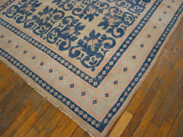 Low-pile rug with geometric patterns in cream, blue, and pale pink rests on warm plank hardwood flooring.