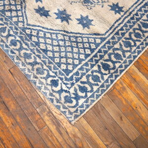 Blue and off-white rug with star motifs and multiple borders rests on warm, distressed hardwood floorboards.