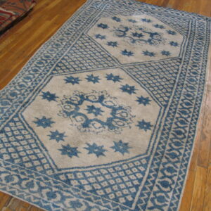 Blue and cream geometric patterned rug rests on polished hardwood planks, visible beside a stack of folded rugs.