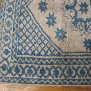 Blue geometric border and star patterns on a high-pile beige rug over wood planks.