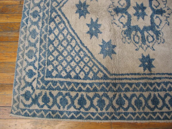 Blue geometric border and star patterns on a high-pile beige rug over wood planks.