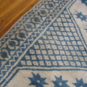 Textured cream and blue geometric patterned rug corner detail on light brown wood floor.