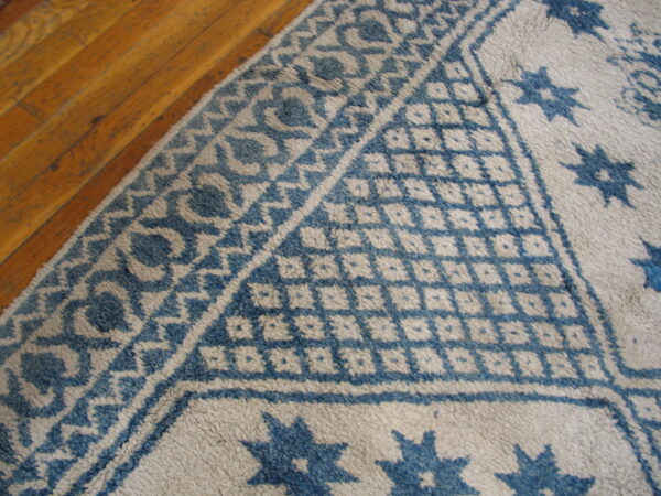 Textured cream and blue geometric patterned rug corner detail on light brown wood floor.
