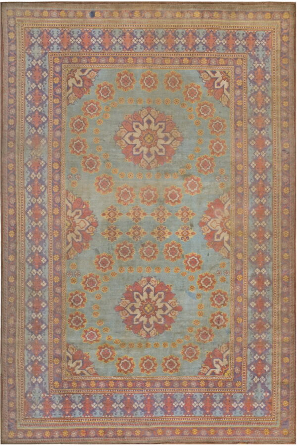 Muted blue field rug with salmon and purple floral medallions surrounded by intricate geometric borders.
