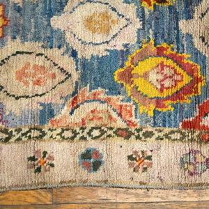 Shaggy blue rug with large abstract yellow, red, and cream motifs rests on light brown wood flooring.