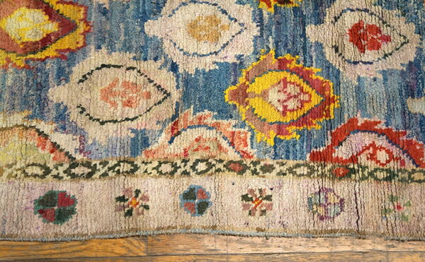 Shaggy blue rug with large abstract yellow, red, and cream motifs rests on light brown wood flooring.