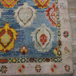 Textured blue rug with bright yellow, red, and white geometric patterns, laid on distressed gray wood planks.