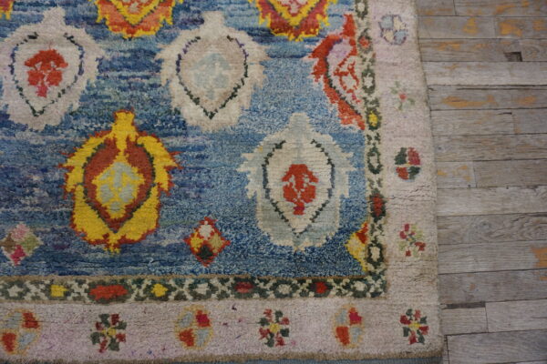 Textured blue rug with bright yellow, red, and white geometric patterns, laid on distressed gray wood planks.