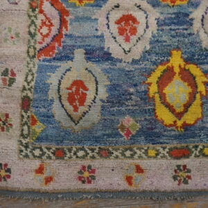 High-pile blue rug with abstract colorful motifs and floral borders rests on light wooden planks.