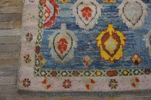 High-pile blue rug with abstract colorful motifs and floral borders rests on light wooden planks.